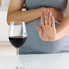 Kobieta w ciąży odrzuca kieliszek czerwonego wina, pokazując dłonią "stop". Alkohol jest szkodliwy dla płodu.