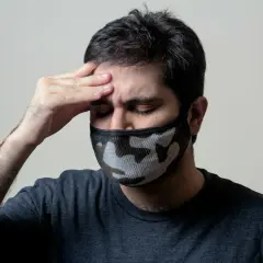 Mężczyzna z maską na twarzy, z ręką na czole, cierpiący na objawy przypominające autoimmunologiczne zapalenie mózgu.