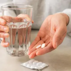 Dłoń trzyma szklankę wody i dwie tabletki. Roticox 60 mg na co pomaga? Na ból i stany zapalne.
