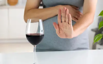 Kobieta w ciąży odrzuca kieliszek czerwonego wina, pokazując dłonią "stop". Alkohol jest szkodliwy dla płodu.