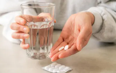 Dłoń trzyma szklankę wody i dwie tabletki. Roticox 60 mg na co pomaga? Na ból i stany zapalne.