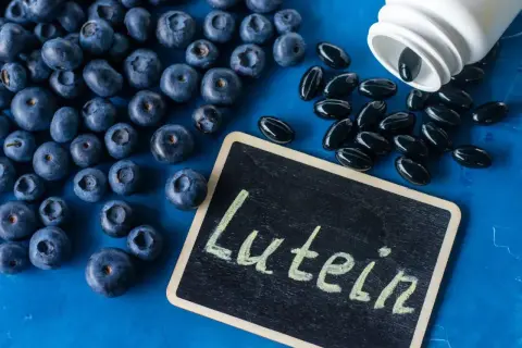 Jagody i kapsułki suplementu diety z napisem "Luteina" na tabliczce. Luteina na oczy wspiera zdrowie wzroku.