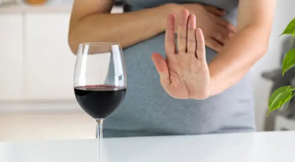 Kobieta w ciąży odrzuca kieliszek czerwonego wina, pokazując dłonią "stop". Alkohol jest szkodliwy dla płodu.