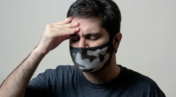 Mężczyzna z maską na twarzy, z ręką na czole, cierpiący na objawy przypominające autoimmunologiczne zapalenie mózgu.