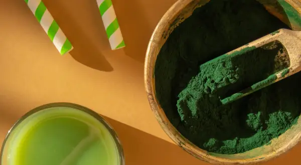 Zielony proszek w drewnianej misce i szklanka napoju. To spirulina – co to jest? Superfood pełen wartości odżywczych.