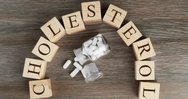 Drewniane klocki układają się w napis "CHOLESTEROL", obok buteleczka z tabletkami, sugerując leczenie.